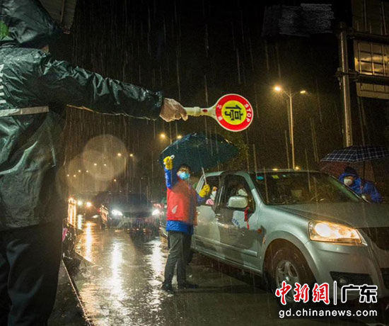 图为清远连州税务的志愿者冒雨值守，在一线交通点为进出人员监测体温。