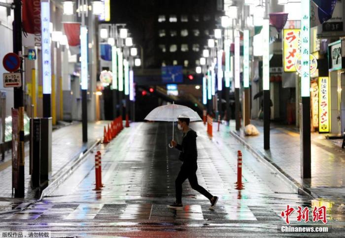 当地时间4月16日晚，日本首相安倍晋三正式宣布，将“紧急事态宣言”适用范围扩展至日本全境，持续时间至5月6日。截至目前，日本境内新冠肺炎病例已超过9000例，东京都单日新增149例，冲绳出现首例死亡病例。日本将从17日起在全国范围内发放布口罩。图为日本东京一名男子戴着口罩在空旷的街头冒雨前行。
